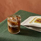 iced coffee in rascal branded glass with terracotta background and green linen table cloth and bag of rascal copy next to it
